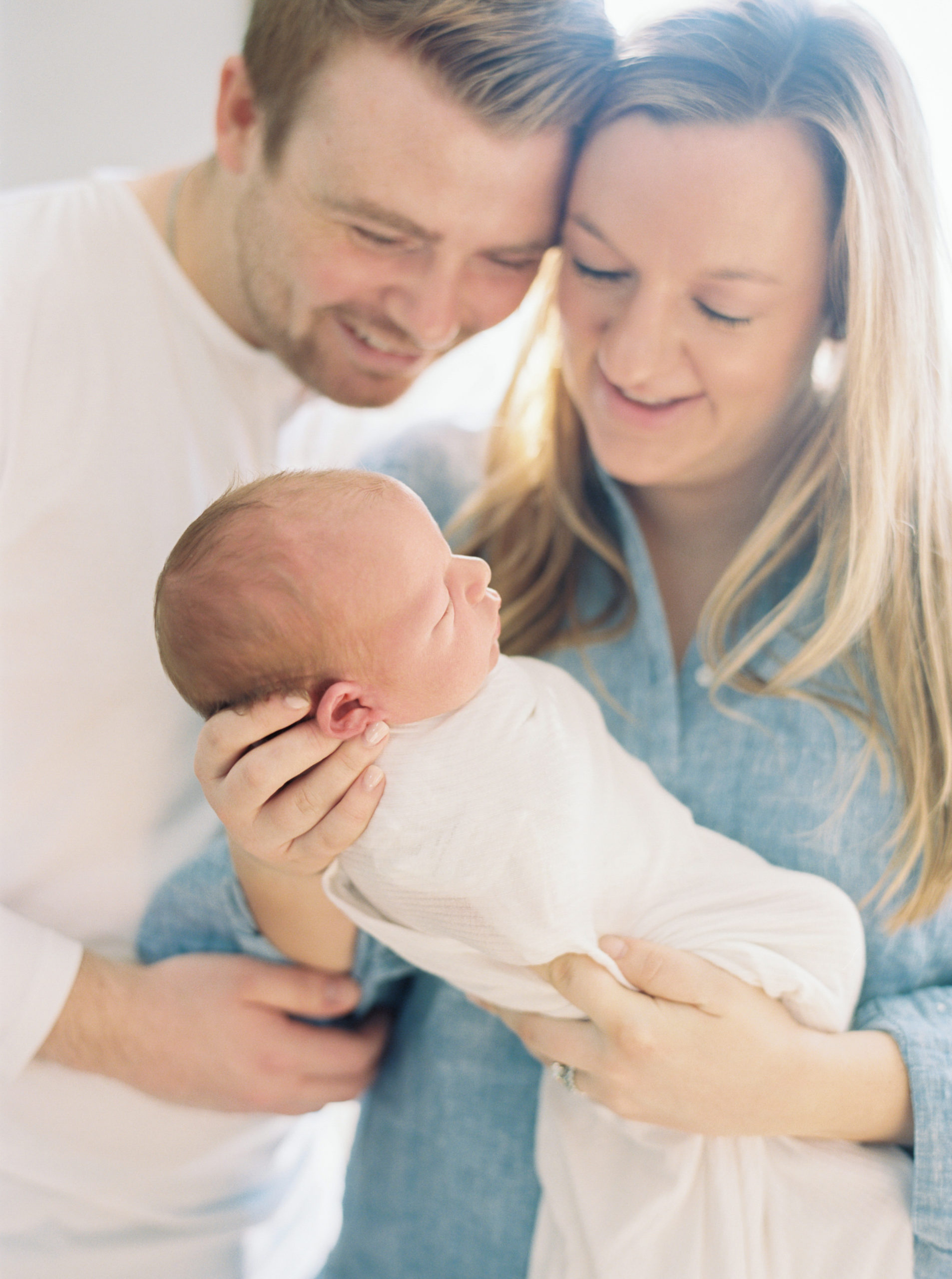 new parents smile at their newborn in window light